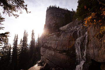 A stunning waterfall cascading down rugged rocks with the setting sun casting a golden glow, creating a breathtaking natural scene with towering cliffs.