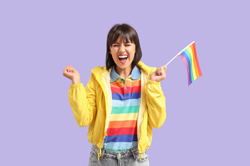 Happy young woman in rainbow t-shirt with LGBT flag on lilac background