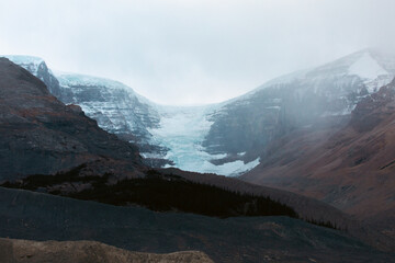 A glacier stretches between two mountains, showcasing the interaction of ice and rock under a clouded sky. It highlights the natural forces shaping the landscape’s rugged beauty.