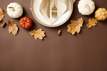 Top view of a festive autumn table setting with white and orange pumpkins, oak leaves, acorns, and...