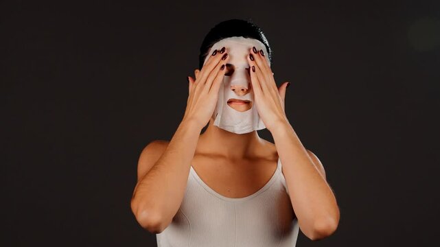 A young woman applies a cosmetic facial mask on a dark background. Homemade facial care concept. Cosmetic mask for facial skin care 4k
