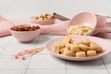 Plate with tasty marzipan candies, almond flakes, nuts and sugar on light tile table