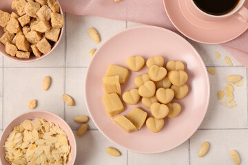 Plates with tasty marzipan candies, almond flakes and cane sugar on light tile background