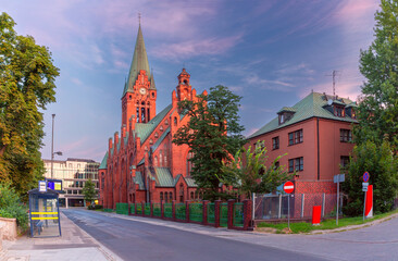 Fototapeta premium View of St. Andrew Bobola Church with a tall spire in Bydgoszcz, Poland, during sunrise, featuring an empty street