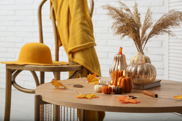 Burning candles in shape of pumpkins, autumn leaves and dry citruses on coffee table at home, closeup