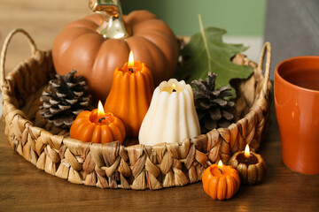 Wicker basket with burning candles in shape of pumpkins, forest bumps and tea cup on coffee table at home, closeup