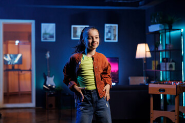 Entertaining generation Z girl dancing and singing while shooting video for social media networks in home interior background. Smiling kid entertaining followers with professional choreography