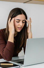 Young adult woman suffering from a headache or migraine due to looking at laptop screen while...