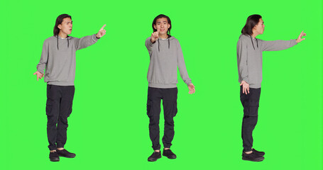 Obraz premium Young adult showing no symbol in studio, expressing negativity and disagreement over isolated greenscreen backdrop. Asian male person being disappointed and disapproving with something.