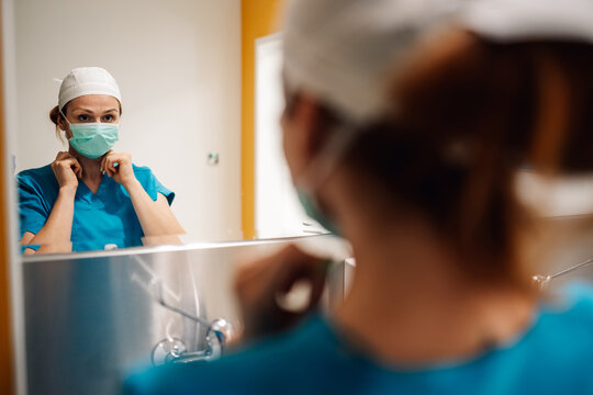 Medical worker fixing mask and cap, focusing in preparation area.