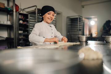 Young girl chef enthusiastically rolling out pastry dough in the kitchen.
