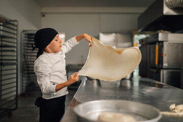 Young girl baker stretching dough in clean kitchen, preparing for baking.
