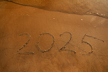 Hand-drawn numbers 2025 of new year on wet yellow sand on beach,