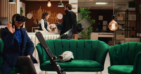Asian person using vr headset in lobby at ski resort, having fun with virtual reality technology before skiing activity on slopes. Woman equipped for winter sports with gear and modern 3d glasses.