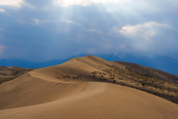 Dramatic desert dunes under sunbeams and cloudy sky