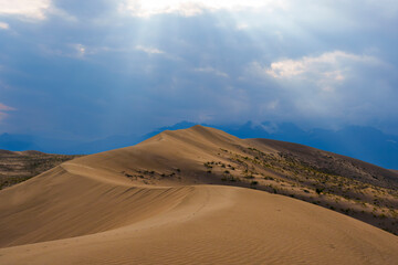 Dramatic desert dunes under sunbeams and cloudy sky