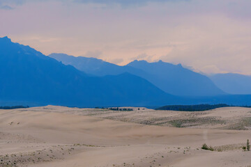 Expansive desert dunes under a dramatic sky with distant mountains