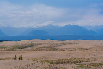 Expansive desert dunes under a dramatic sky with distant mountains