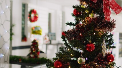 Close up shot of beautifully decorated Christmas pine tree with empty office in blurry background. Xmas tree adorn with red bows and baubles in festive workplace during winter holiday season