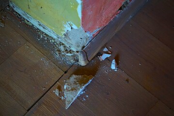 Uszkodzona ściana w starym domu. Odpadający tynk od ściany. Pokruszony tynk i ściana w dwóch kolorach. Dom wymagający natychmiastowego remontu. © Adam