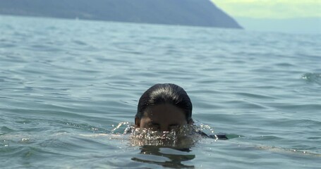 Slow-motion of a woman emerging from water with serene expression, water droplets cascading from her face, surrounded by the vast ocean, capturing the beauty of nature and tranquility