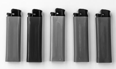 Plastic lighters with mechanical ignition, a compact object, located in one line. Black and white horizontal photo from top to bottom.