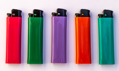 Five lighters of different colors, pink, green, purple, orange and blue lie on a white background