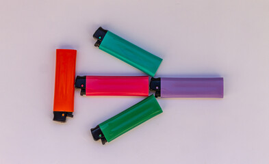 Five lighters of different colors, pink, green, purple, orange and blue lie on a white background