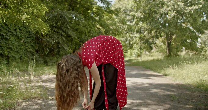 A young woman wearing a red polka dot dress dances modern interpretive dance in a sunny park.