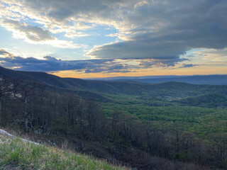 At dusk, Skyline Drive in Shenandoah National Park reveals rolling green hills bathed in soft blue and purple hues. The fading light casts a peaceful glow over the landscape as day turns to night.
