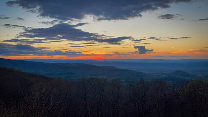 A stunning orange and yellow sunset blankets the horizon from Skyline Drive in Shenandoah National Park, casting a golden glow over the rolling mountains, as the fading light transforms the evening.