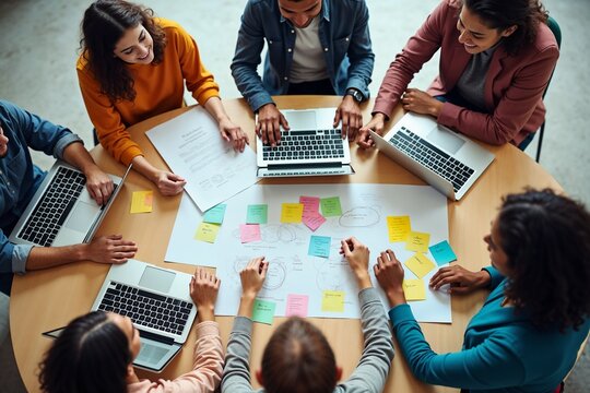 A diverse team engages in a brainstorming session around a table filled with laptops, sticky notes, and papers, representing collaboration, creativity, and planning in a modern workspace.