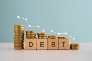 DEBT word on wooden cube blocks word and down arrow with stack of coins for financial debt decrease concept
