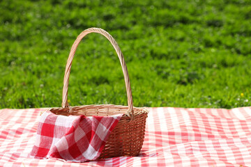 One picnic wicker basket with checkered napkin and blanket on green grass. Space for text