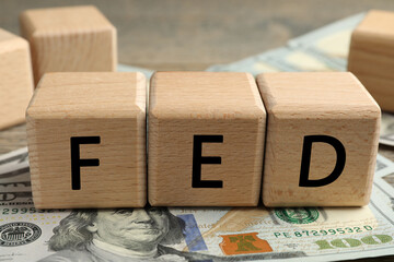 Wooden cubes with letters Fed (Federal Reserve System) and dollar banknotes on table, closeup