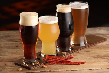 Glasses with different types of beer and snacks on wooden table indoors