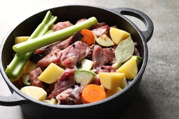 Cooking stew. Uncooked meat and vegetables in pot on light grey table, closeup