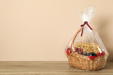 Wicker gift basket on wooden table against beige background. Space for text