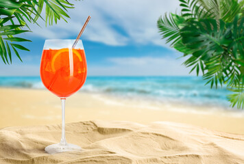 Summer beach with Aperol Spritz delicious cocktail, tropical leaves and golden sand