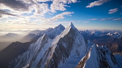 Rugged mountain peaks tower majestically against a backdrop of scattered clouds, with sunlight illuminating snow-covered cliffs and deep valleys below, creating a stunning landscape