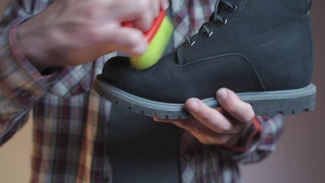 Man cleaning black boots with brushes in the studio. Male brushing nubuck footwear with a small scrub brush. Theme of care for winter shoes. Washes dirty black fall booties, workshop shoes cleaner. 