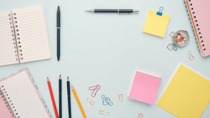 A vibrant collection of stationery supplies including notebooks, pens, and sticky notes arranged on a light blue desk