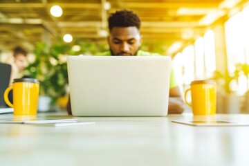 Focused African American Male Engineer Using Laptop in Modern Open-Plan Office with Colleagues, Showcasing Teamwork and Technology
