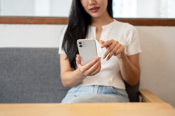 Fototapeta premium A close-up of a beautiful Asian woman sitting on a sofa in a coffee shop, using her smartphone.