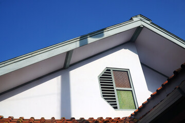 Part of the house, top floor, roof ridge, and roof ventilation - against the background of a clear blue sky horizontally. Copy space