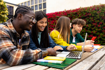 Happy multiracial college students outdoors in college campus studying using laptop.
