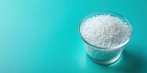 Top view of plastic polypropylene granules in a glass cup on cyan backdrop , masterbatch, polymer, HDPE, PVC, resin
