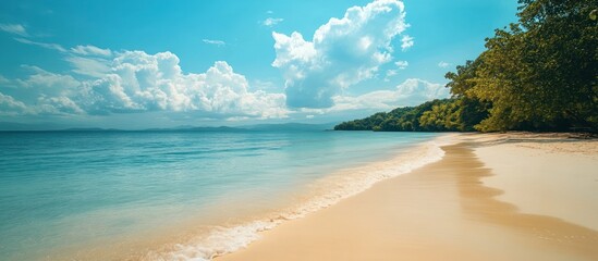 Obraz premium A beautiful tropical beach with white sand, clear blue water, and lush green trees on a sunny day with fluffy clouds.