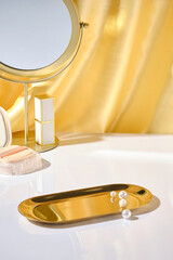 Empty bronze tray displayed on white table with some pearls decorated, some cosmetic for make up...
