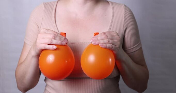 A woman holds deflated balloons demonstrating the concept of breast modification after feeding a baby and reaching age. High quality 4k footage
